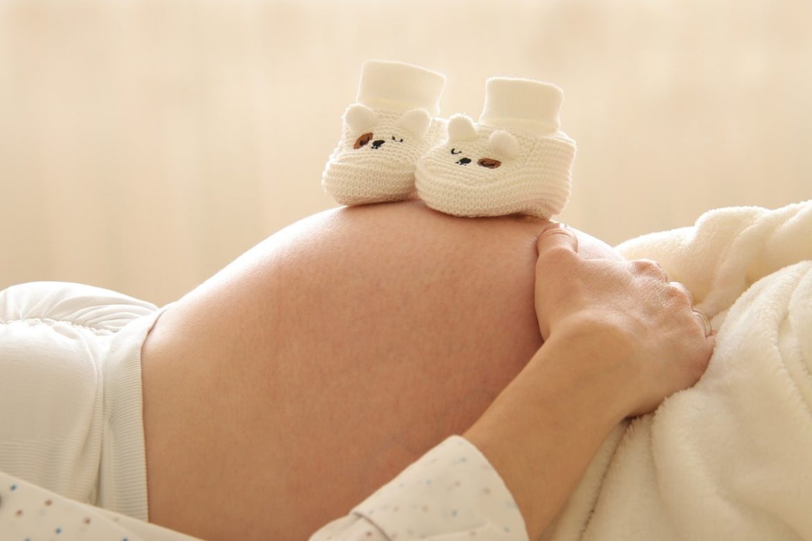 Ventre de femme enceinte avec chaussons de bébé et faisant possiblement l'usage de Bolas de Grossesse pour le bien-être.