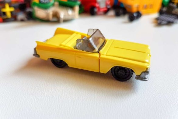 Une voiture miniature décapotable jaune est posée sur une surface blanche.