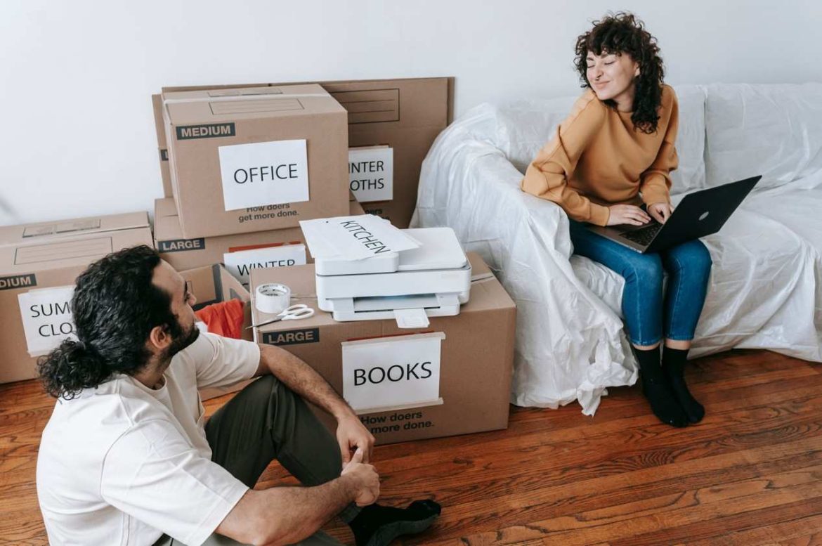 Un couple organise ses cartons étiquetés par catégories comme les livres ou le bureau, illustrant la différence entre carton standard et carton livre déménagement dans un salon.