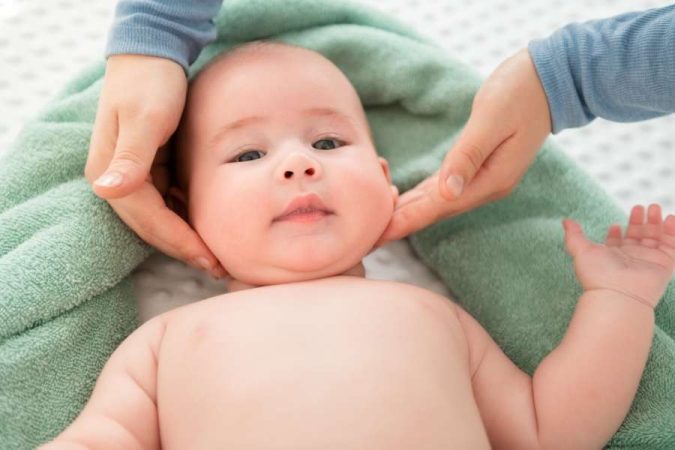 Un parent en train de masser doucement le visage d'un bébé allongé sur une serviette.