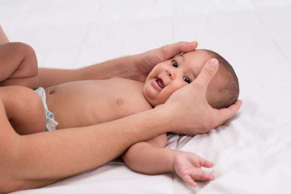 Un adulte qui soutient et masse le visage d'un bébé souriant.