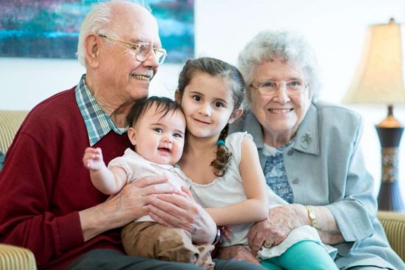 Des grands-parents bienveillants posent joyeusement avec leurs jeunes petits-enfants dans un intérieur lumineux.