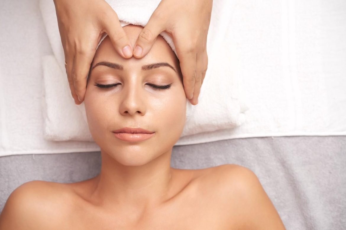 Femme allongée recevant un massage facial japonais jeunesse de la peau avec des pressions ciblées sur le front et les tempes.
