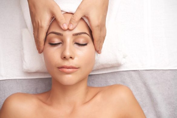 Femme allongée recevant un massage facial japonais jeunesse de la peau avec des pressions ciblées sur le front et les tempes.